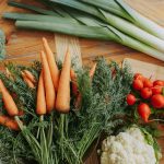 A colorful assortment of fresh vegetables including carrots, leeks, and radishes displayed on a wooden table.