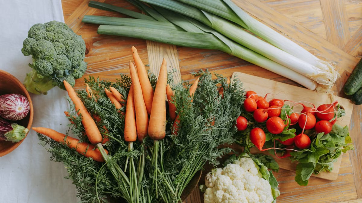 A colorful assortment of fresh vegetables including carrots, leeks, and radishes displayed on a wooden table.